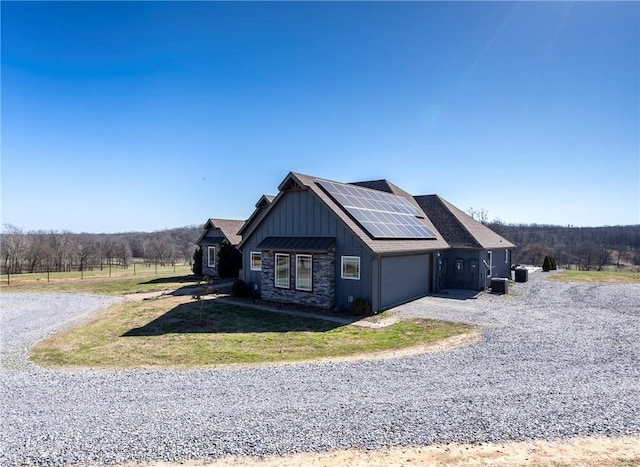 view of side of property with solar panels, board and batten siding, driveway, stone siding, and an attached garage