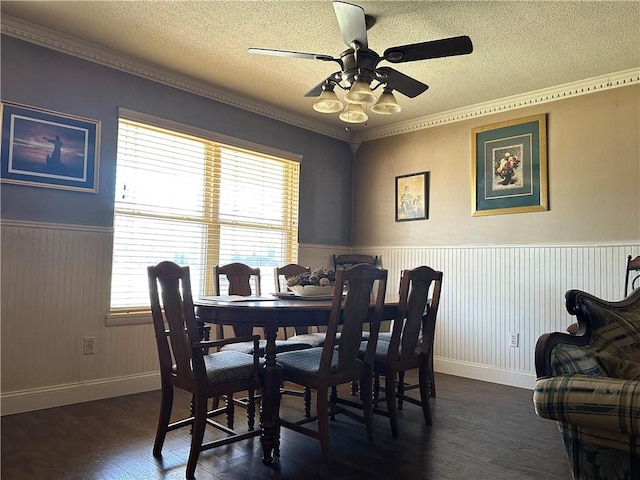 dining area featuring a ceiling fan, dark wood-style flooring, wainscoting, ornamental molding, and a textured ceiling