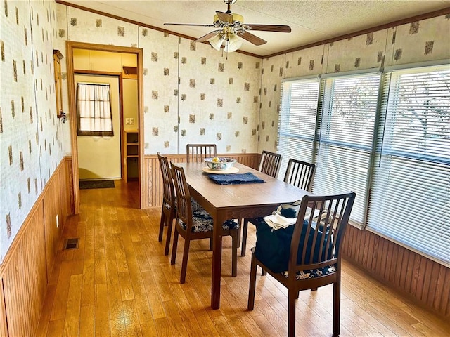 dining space featuring a wainscoted wall, visible vents, wallpapered walls, crown molding, and light wood-type flooring