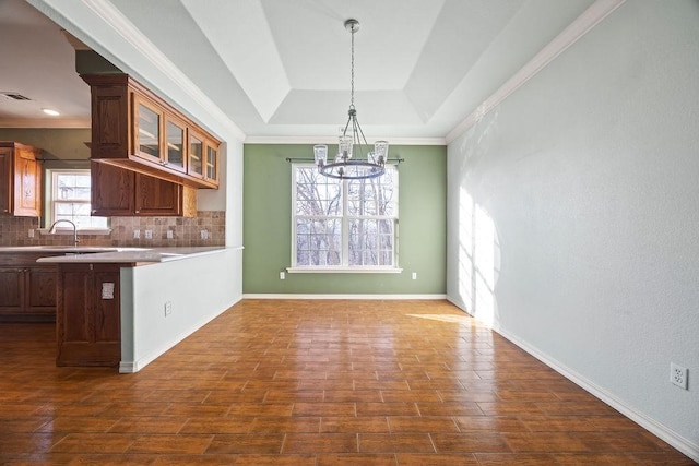 kitchen with decorative backsplash, a tray ceiling, a notable chandelier, and glass insert cabinets