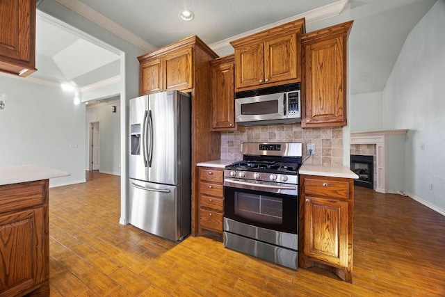 kitchen featuring brown cabinets, backsplash, stainless steel appliances, crown molding, and light countertops