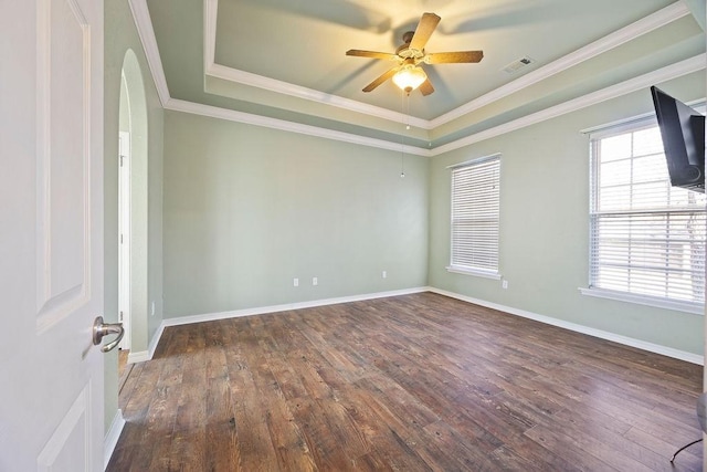 empty room with a tray ceiling, wood finished floors, visible vents, and baseboards