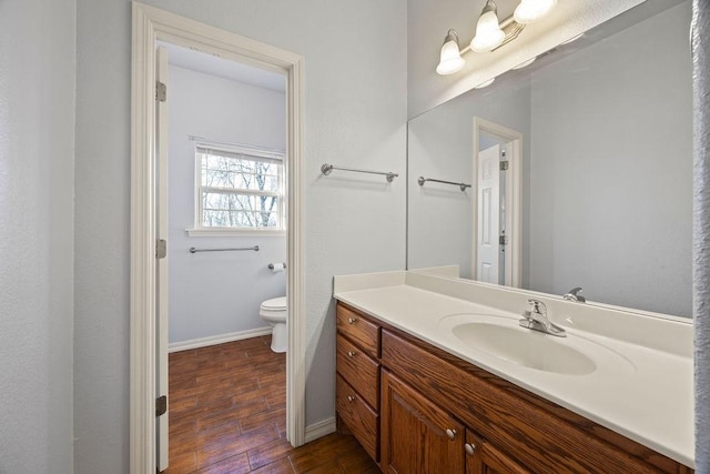 bathroom with vanity, toilet, wood finished floors, and baseboards