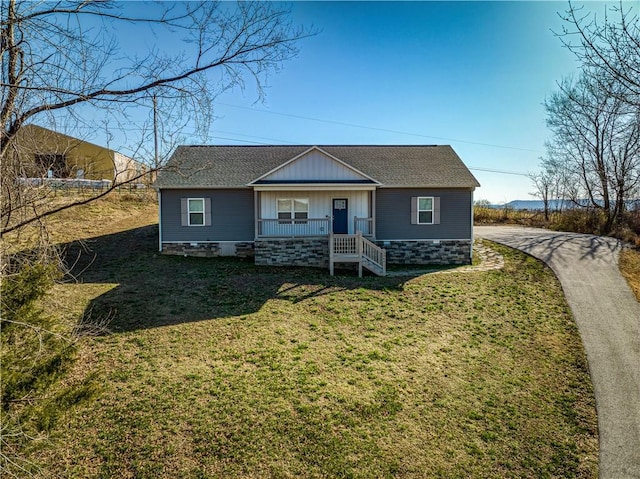 view of front facade featuring board and batten siding, a shingled roof, a porch, a front yard, and stone siding