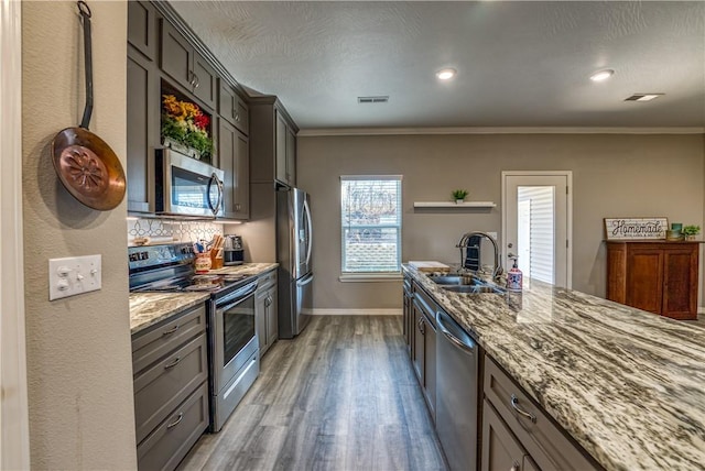 kitchen with light wood finished floors, appliances with stainless steel finishes, light stone countertops, and a sink