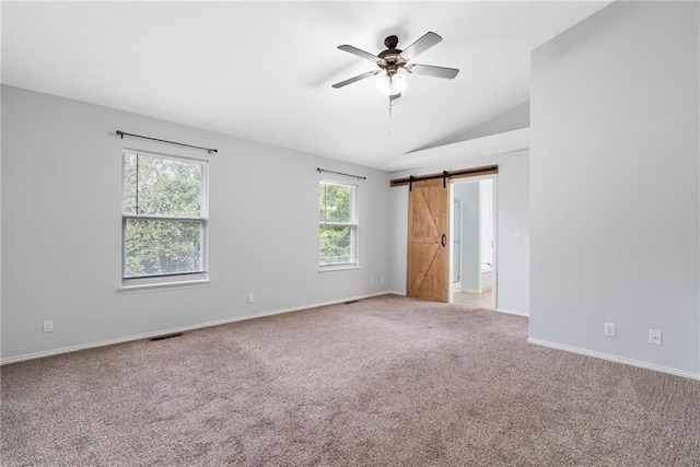 carpeted spare room featuring visible vents, baseboards, a barn door, lofted ceiling, and a ceiling fan