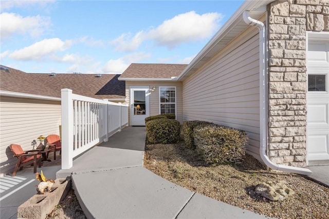 view of exterior entry featuring an attached garage and a shingled roof