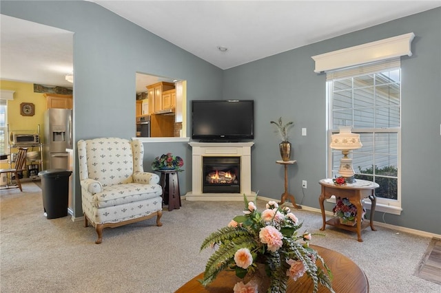 living area with plenty of natural light, light colored carpet, lofted ceiling, and a glass covered fireplace