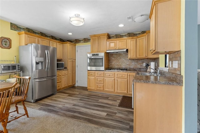 kitchen featuring visible vents, under cabinet range hood, a sink, dark countertops, and stainless steel appliances