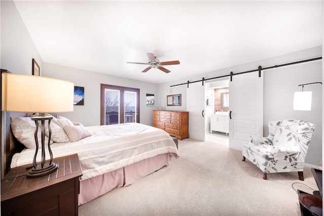 carpeted bedroom featuring ensuite bath, a barn door, and a ceiling fan