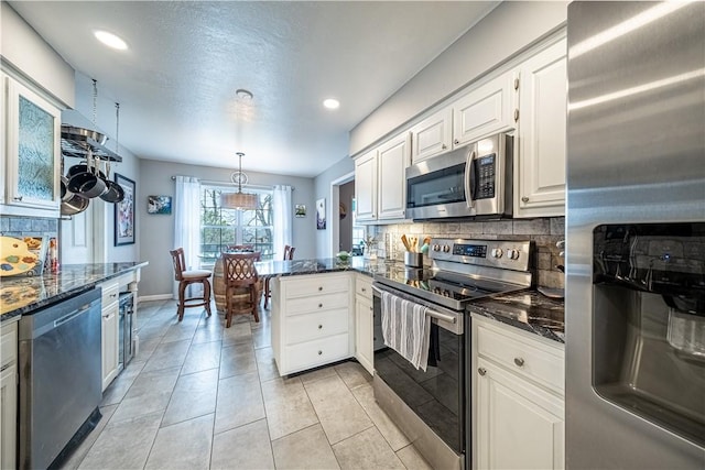 kitchen with white cabinets, a peninsula, stainless steel appliances, and dark stone countertops