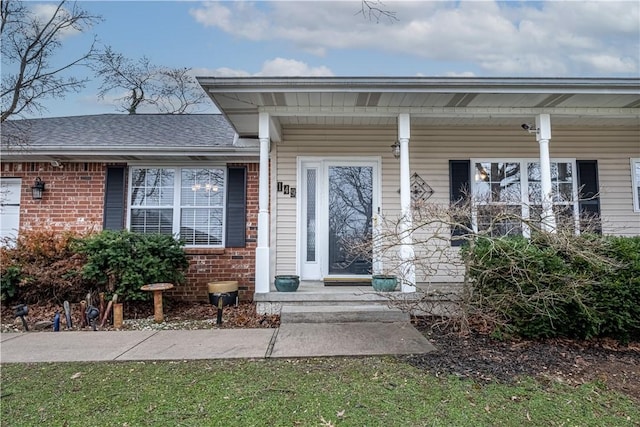 view of exterior entry with brick siding and a shingled roof