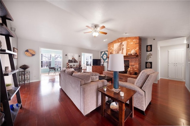 living room featuring a fireplace, vaulted ceiling, dark wood-style floors, and ceiling fan