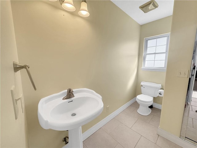 half bath with tile patterned flooring, toilet, baseboards, and a sink