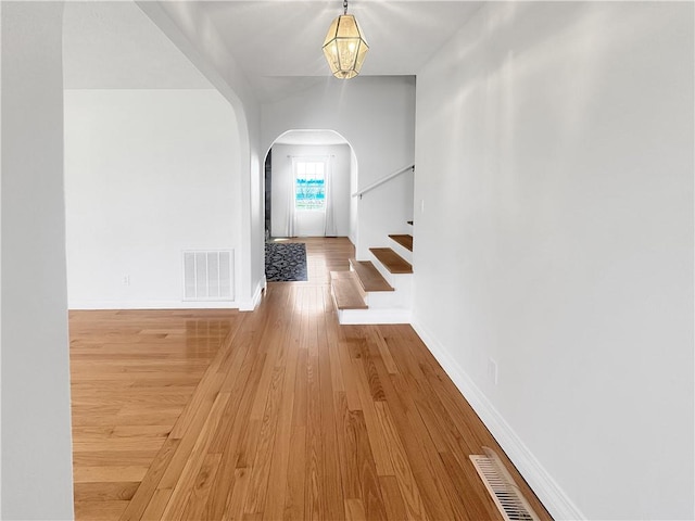 hallway with wood finished floors, visible vents, baseboards, arched walkways, and stairs