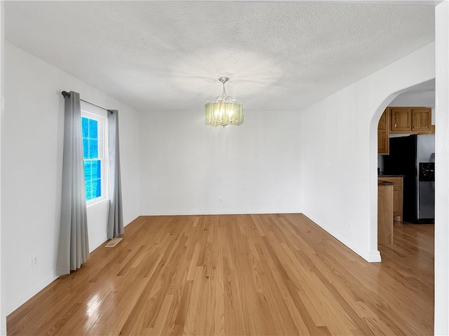 spare room with light wood-type flooring, arched walkways, a textured ceiling, and a chandelier