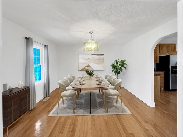 unfurnished dining area with visible vents, arched walkways, light wood-style floors, a textured ceiling, and a chandelier