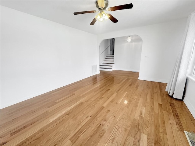 unfurnished living room with visible vents, baseboards, light wood-style floors, arched walkways, and a ceiling fan