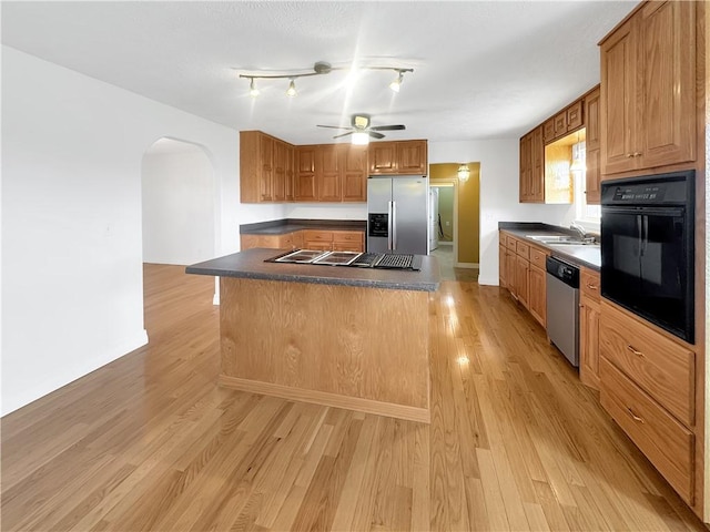 kitchen with black appliances, a ceiling fan, dark countertops, arched walkways, and light wood-style floors