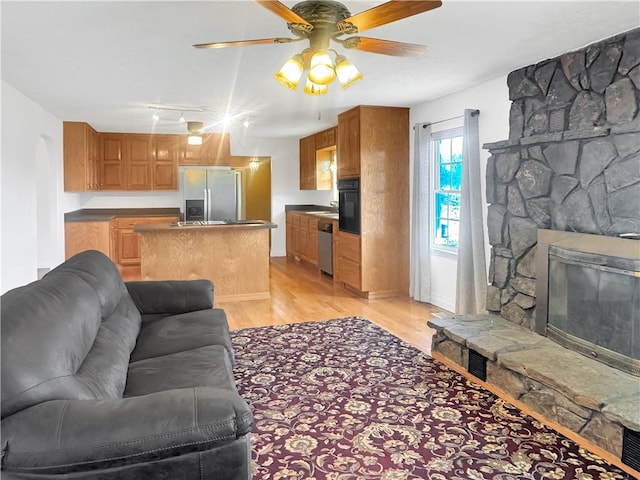 living area featuring light wood-type flooring, a stone fireplace, and ceiling fan