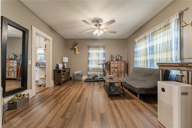 living area with ceiling fan, wood finished floors, and crown molding