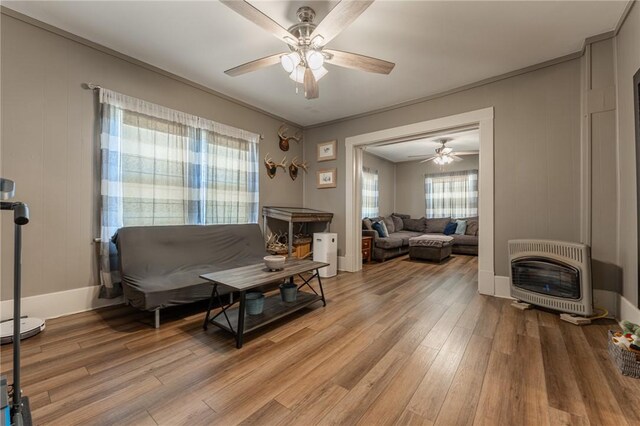 living area with heating unit, a ceiling fan, light wood-type flooring, and baseboards