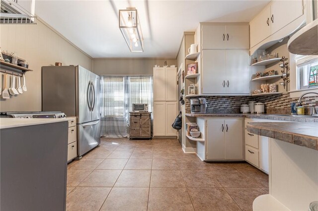 kitchen featuring light tile patterned floors, open shelves, freestanding refrigerator, dark countertops, and backsplash