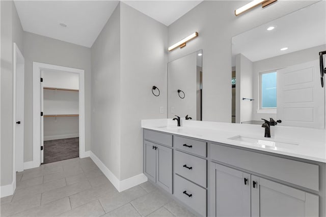 full bath featuring double vanity, baseboards, a sink, and a walk in closet