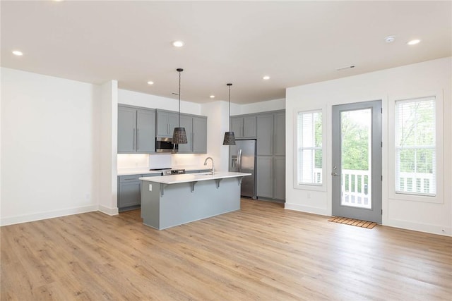 kitchen featuring light wood finished floors, gray cabinetry, a breakfast bar area, light countertops, and appliances with stainless steel finishes