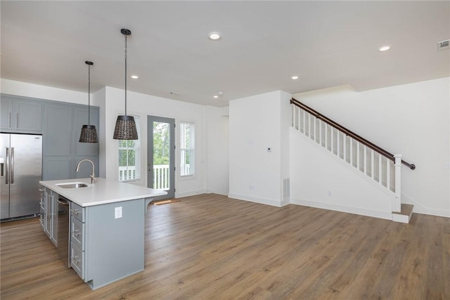 kitchen with light wood finished floors, recessed lighting, gray cabinets, stainless steel refrigerator with ice dispenser, and a sink