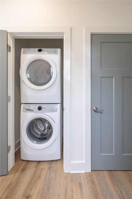 clothes washing area with stacked washer and clothes dryer, light wood-style flooring, and laundry area