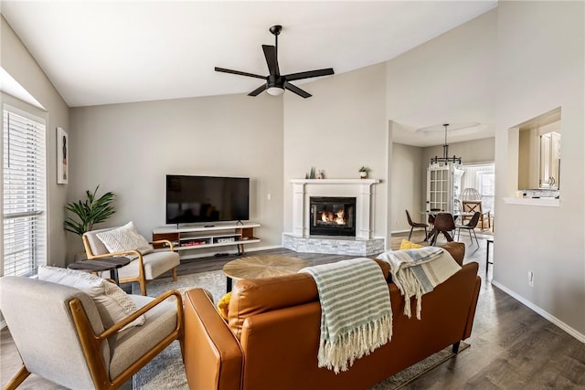 living room featuring dark wood-type flooring, baseboards, lofted ceiling, ceiling fan with notable chandelier, and a glass covered fireplace