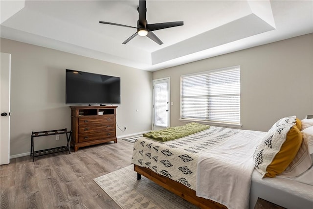 bedroom with baseboards, a raised ceiling, wood finished floors, and a ceiling fan