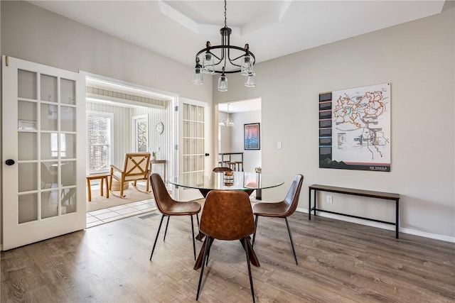 dining space with wood finished floors, baseboards, a tray ceiling, french doors, and a chandelier