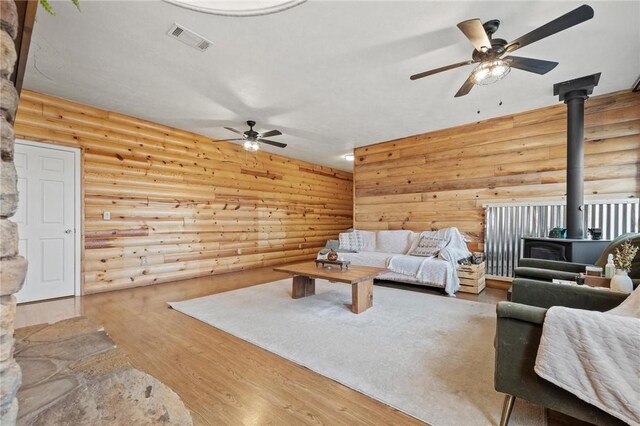 unfurnished living room with visible vents, log walls, a wood stove, and wood finished floors