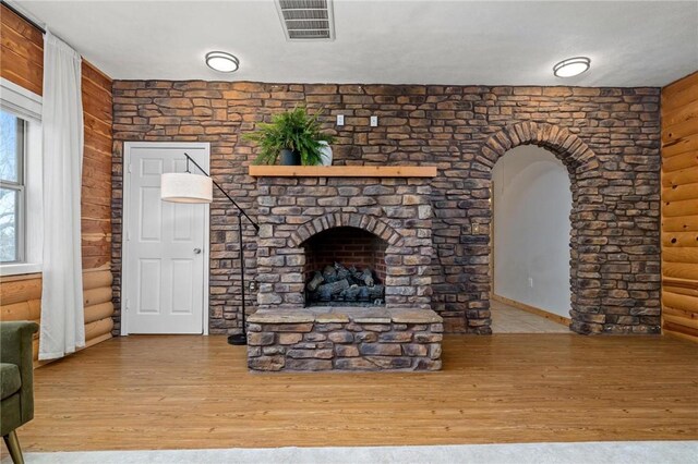 living area featuring visible vents, a fireplace with raised hearth, wood finished floors, arched walkways, and log walls