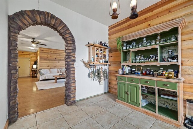 bar with wooden walls, light tile patterned flooring, a ceiling fan, and arched walkways