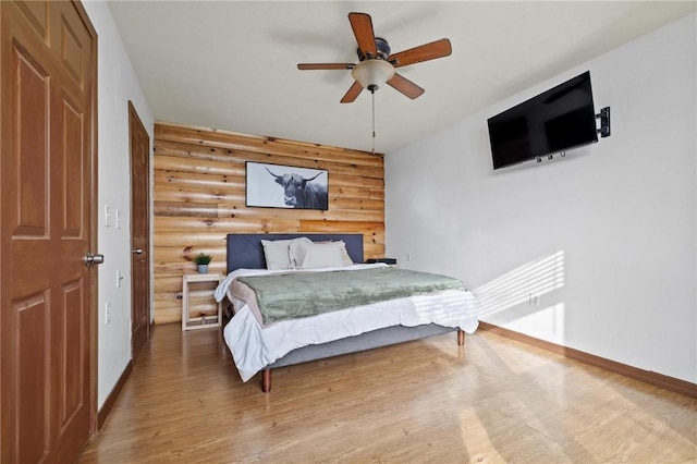 bedroom with ceiling fan, log walls, baseboards, and wood finished floors