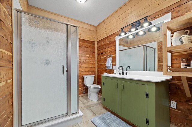 bathroom with tile patterned flooring, wood walls, toilet, a stall shower, and vanity