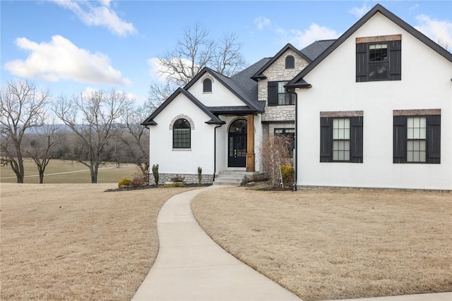 view of front of house featuring a shingled roof, stone siding, and stucco siding