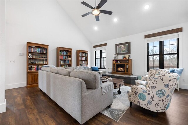 living room with a wealth of natural light, high vaulted ceiling, a warm lit fireplace, and dark wood-style floors