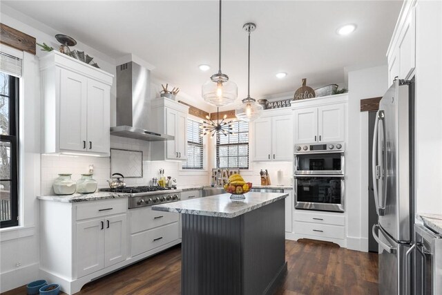 kitchen featuring backsplash, white cabinets, stainless steel appliances, and wall chimney range hood