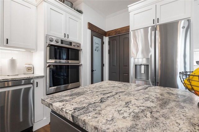 kitchen with ornamental molding, appliances with stainless steel finishes, white cabinets, decorative backsplash, and light stone countertops