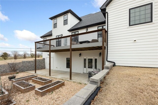 back of house with a patio, roof with shingles, and a vegetable garden