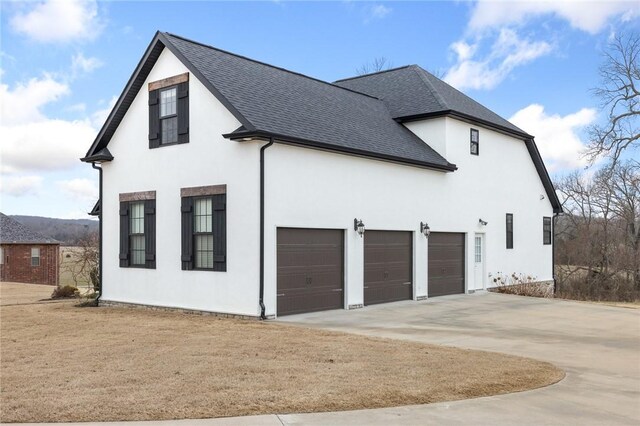 view of side of home featuring stucco siding, an attached garage, driveway, and a shingled roof