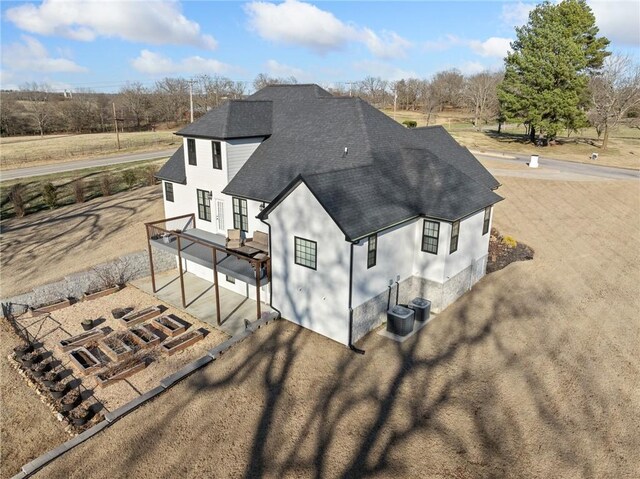 rear view of property featuring dirt driveway, cooling unit, roof with shingles, and stucco siding