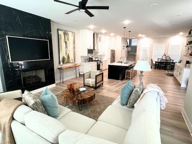 living room with light wood finished floors, baseboards, a high end fireplace, and ceiling fan