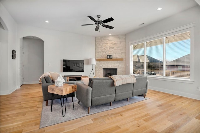 living room featuring baseboards, light wood-type flooring, recessed lighting, a fireplace, and arched walkways