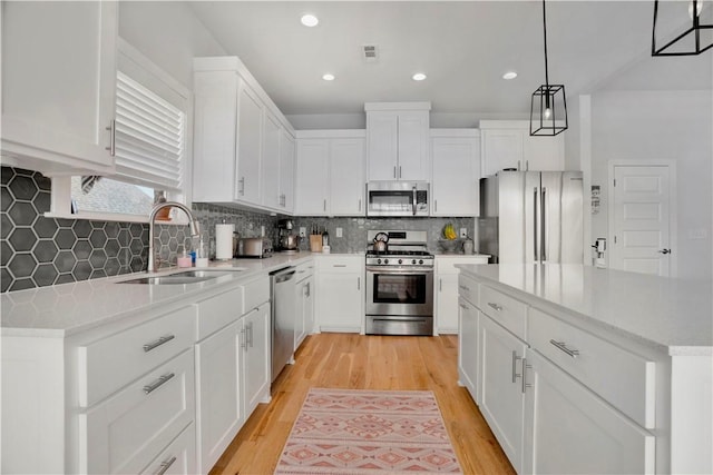 kitchen featuring light wood finished floors, decorative backsplash, white cabinets, stainless steel appliances, and a sink