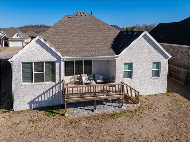 back of property with brick siding, a shingled roof, a deck, and fence